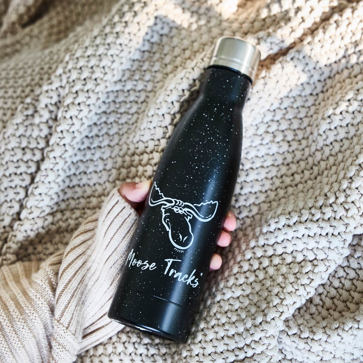 A person holding a black Moose Tracks Water bottle that reads, "Moose Tracks" and features a moose head logo on the front.