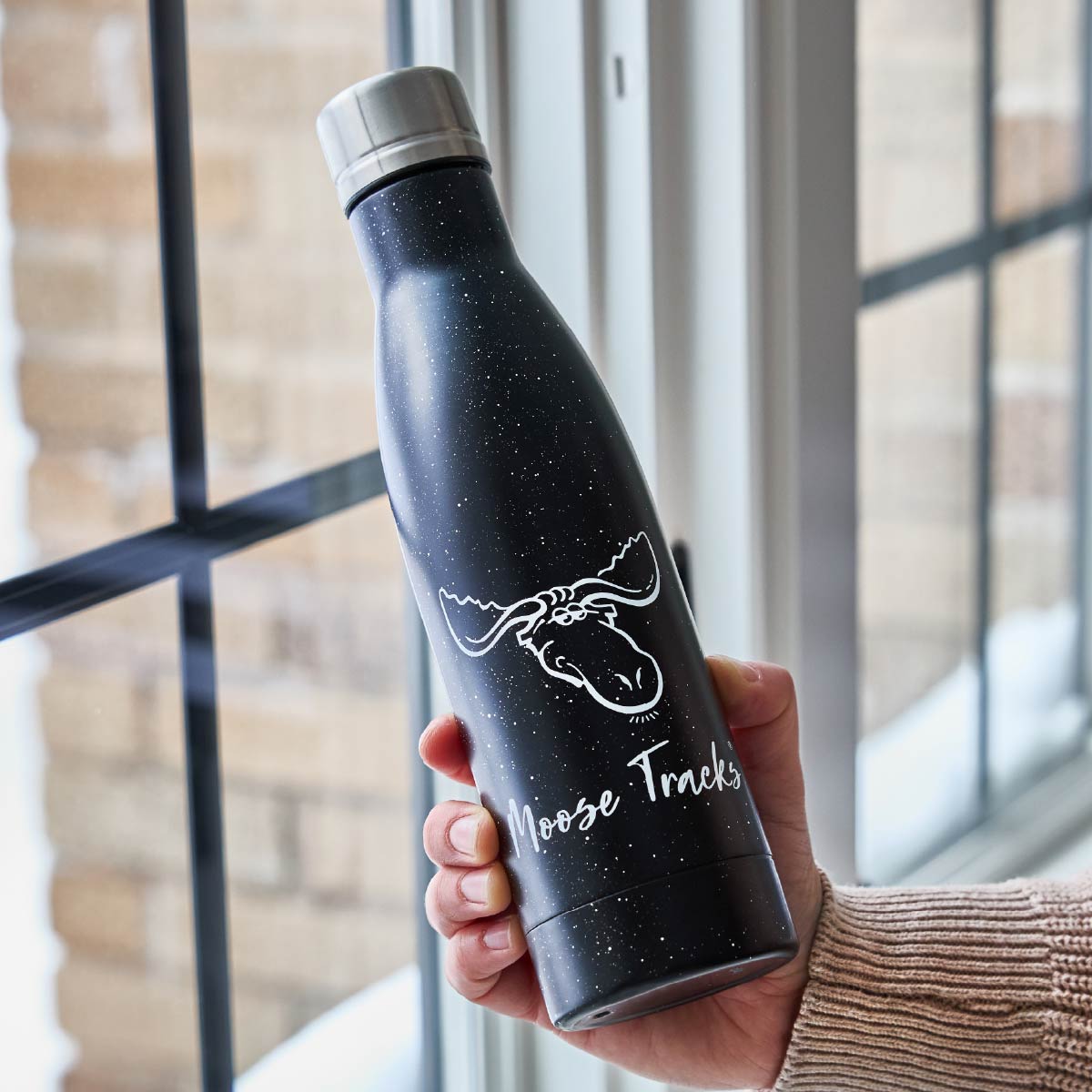 A person holding a black Moose Tracks Water bottle that reads, "Moose Tracks" and features a moose head logo on the front.