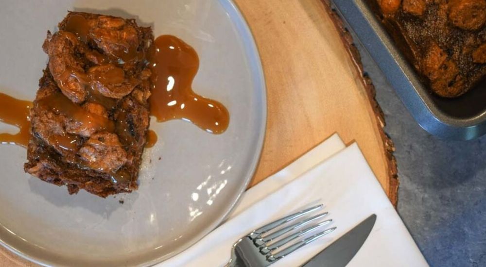 Moose Tracks bread pudding covered in caramel sauce sitting on a grey plate