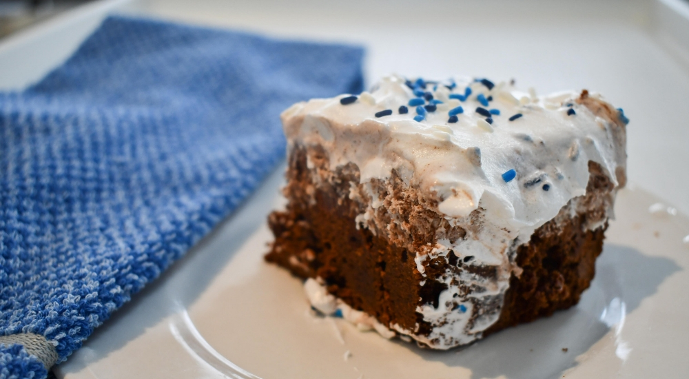 Moose Tracks Brownie Layer Cake with a whipped cream frosting. Sitting on a plate with a blue towel next to it.