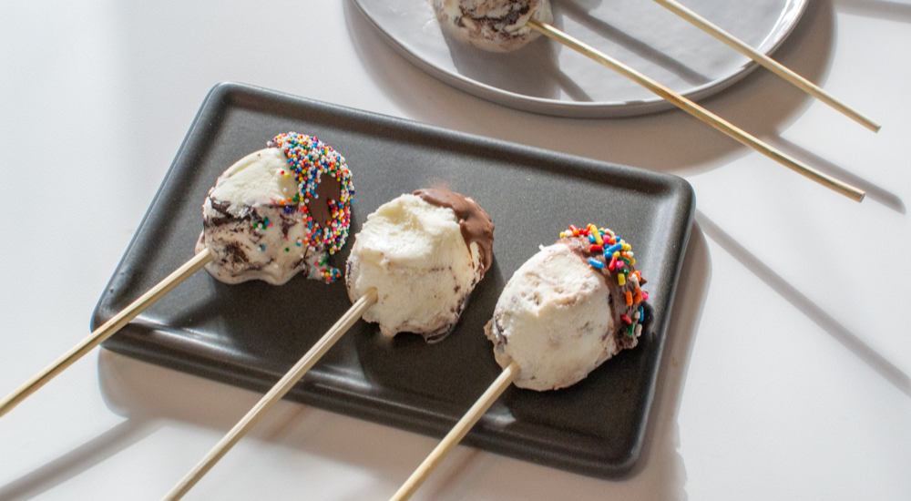 Scoops of ice cream in the shape of Easter eggs on a plate with skewers.