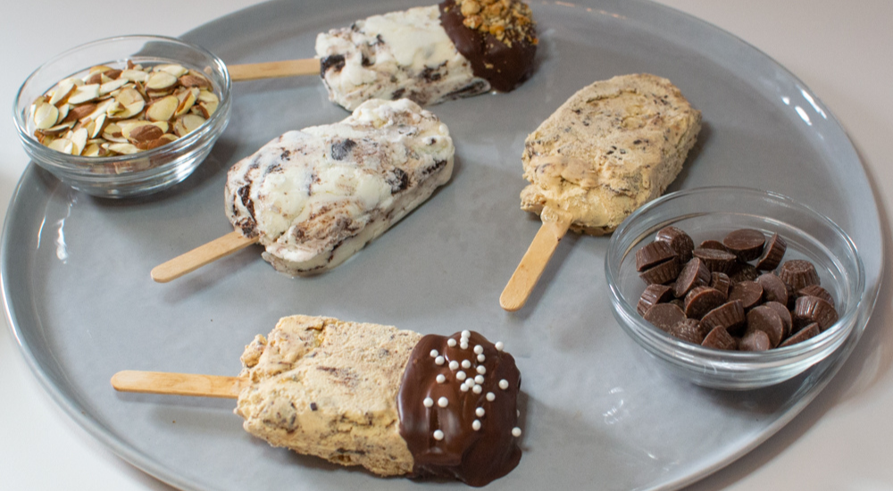 Four Moose Tracks Ice Cream Bars on a plate with peanut butter cups and chopped peanuts in small bowls next to them.