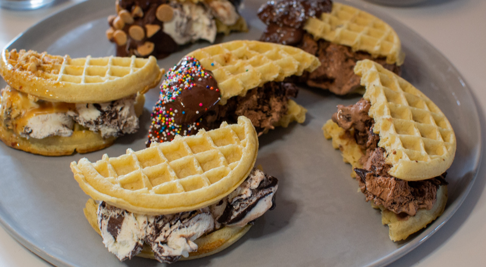 Multiple waffle ice cream sandwiches sitting on a plate.