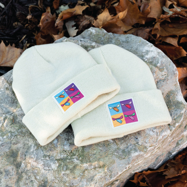 two tan winter beanies with moose tracks pop art logo on the cuff laying outside on a rock