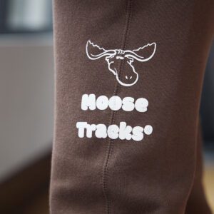A close-up picture of vanilla-colored screen printing on brown sweatpants, which reads, "Moose Tracks," and a moose icon