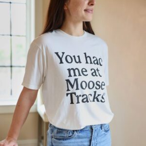 A woman wearing jeans and a light-colored t-shirt with "You had me at Moose Tracks" printed on the front.