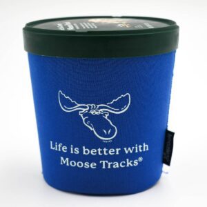 An ice cream pint with a Moose Tracks Ice Cream Koozie standing upright. The koozie is blue with a Moose Tracks logo and text reading "Life is Better with Moose Tracks" in white-colored screen printing.
