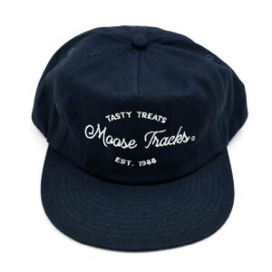 An aerial view of the Moose Tracks Navy Snapback Hat placed on a flat surface and white background. The hat is navy with white-colored embroidered text reading "Tasty Treats Moose Tracks EST. 1988".