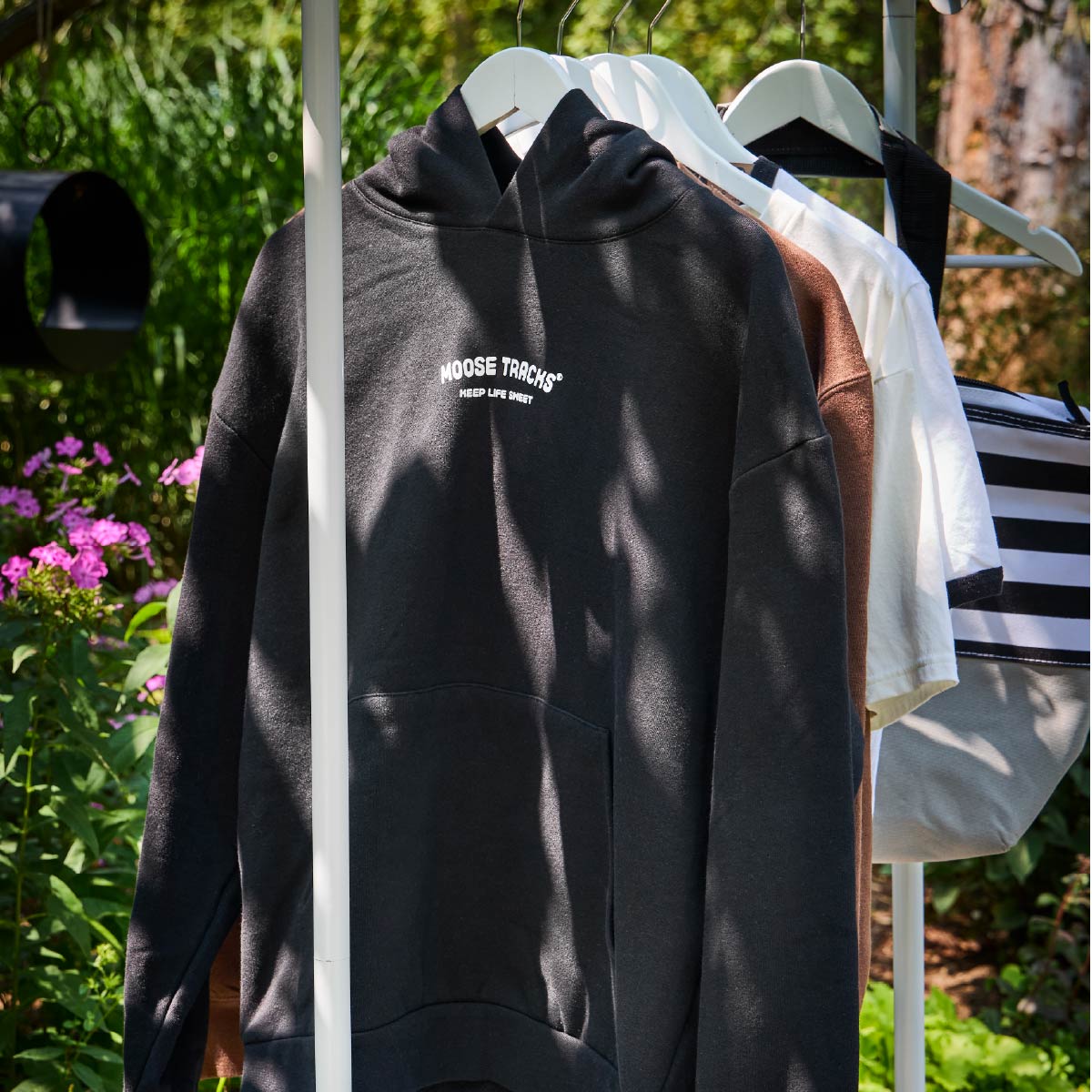 A black hoodie hanging on a hanger and clothes rack that reads, "Keep life sweet".