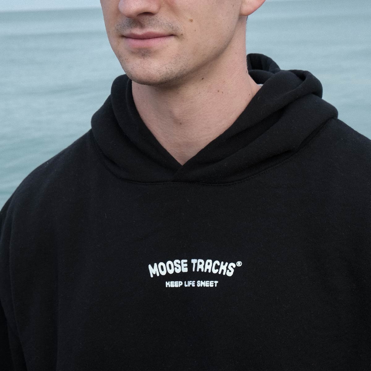 A man wearing the Moose Tracks Keep Life Sweet Hoodie. The sweatshirt is black and reads, "Moose Tracks Keep Life Sweet" in white text on the chest.